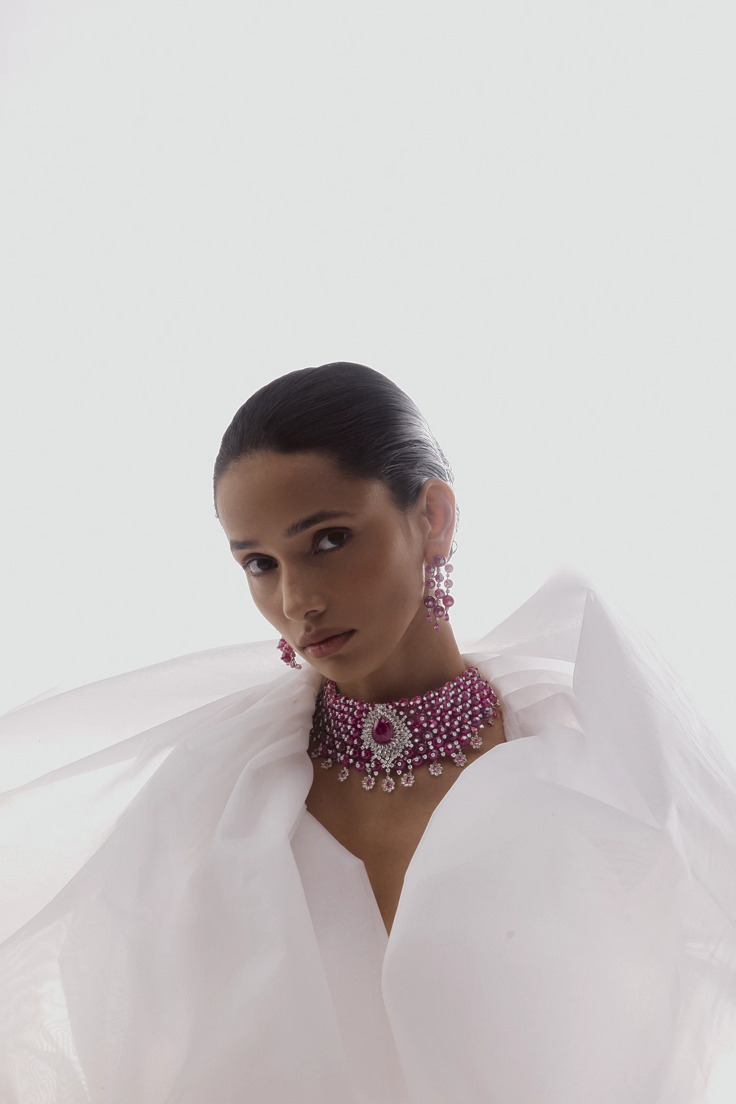 Model in white organza looking into the camera, wearing a pink spinel choker and cascading earrings.
